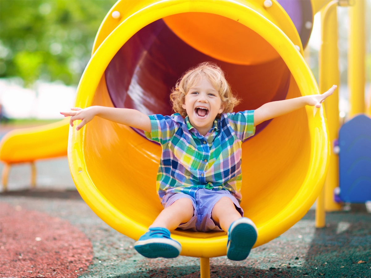 child at bottom of slide smiling with hands out wide open