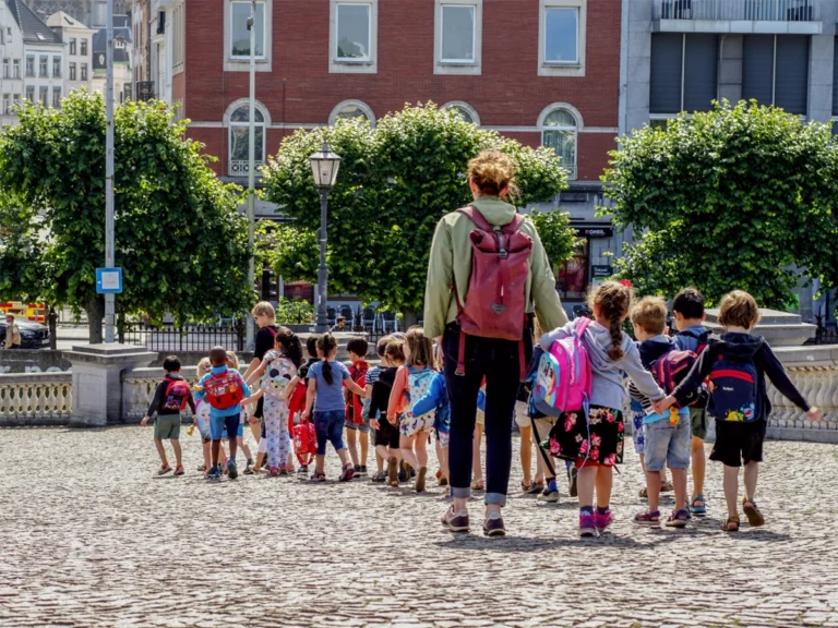 A Teacher guides her students while walking in the city.